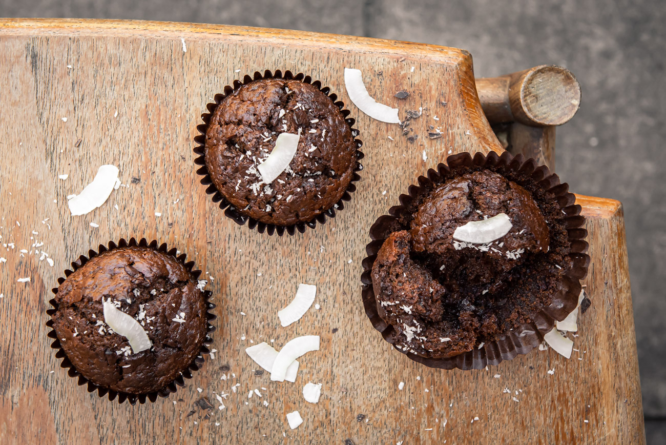 Three chocolate muffins on a light wooden table, top down view