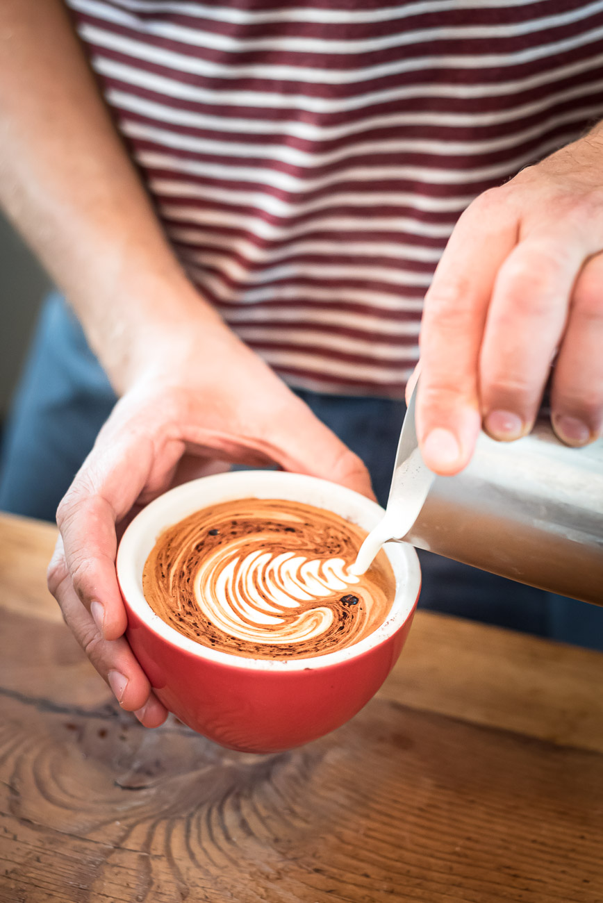 Barista pouring milk to create latte art on a cappuccino