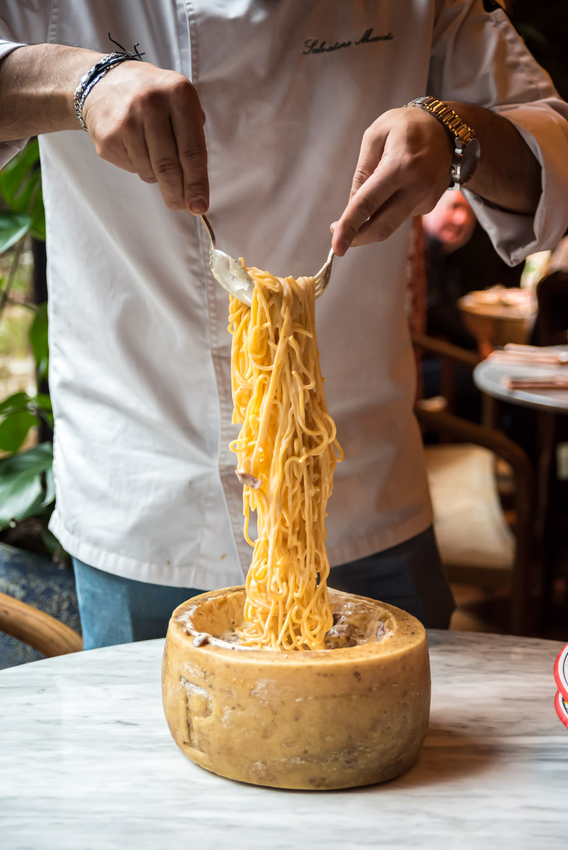 Chef pulling spaghetti alla carbonara out of a cheese wheel